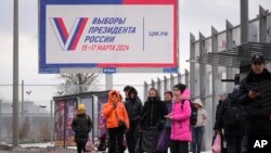 Ljudi čekaju autobus na autobuskoj stanici pored bilborda koji promoviše predstojeće predsjedničke izbore, u Sankt Peterburgu, Rusija, 20. decembra , 2023.