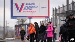 Oamenii așteaptă într-o stație de autobuz din Sankt Petersburg lângă un panou publicitar care promovează viitoarele alegeri prezidențiale din Rusia.