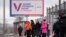 Oamenii așteaptă într-o stație de autobuz din Sankt Petersburg lângă un panou publicitar care promovează viitoarele alegeri prezidențiale din Rusia.