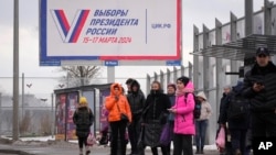 Ljudi čekaju na autobuskoj stanici pokraj velikog plakata koji promoviše nadolazeće predsjedničke izbore u Sankt Peterburgu, decembar 2023. 