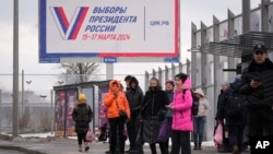 Люди на автобусной остановке в Санкт-Петербурге на фоне билборда с информацией о дате президентских выборов в России. Декабрь 2023 года