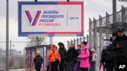 People wait at a bus stop next to a billboard promoting the upcoming presidential election in St. Petersburg in December.