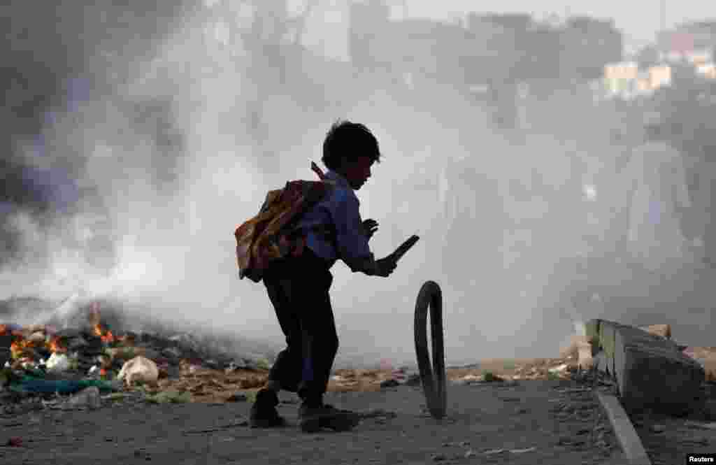 A boy plays with a tire near garbage being set on fire by residents of a slum in Karachi, Pakistan.