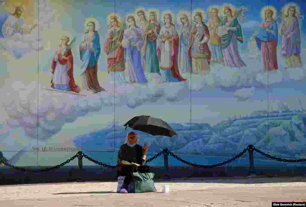A woman sits under an umbrella and begs for money during a sunny day in front of the St. Michael&#39;s Golden-Domed Cathedral in Kyiv. (Reuters/Gleb Garanich)