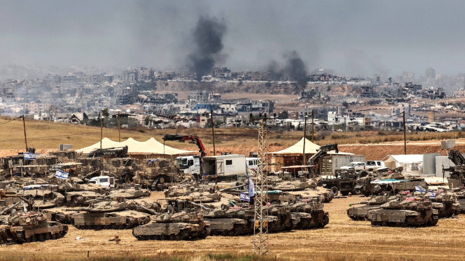 This picture taken from a position in southern Israel on the border with the Gaza Strip shows Israeli tanks and bulldozers deployed as smoke billows over destroyed buildings in Gaza during Israeli bombardment on May 17, 2025.