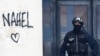 Një oficer policie franceze siguron hyrjen e një ndërtese teksa qëndron pranë emrit "Nahel''', i spërkatur në mur gjatë protestave në Nante, në Francën perëndimore më 30 qershor 2023.