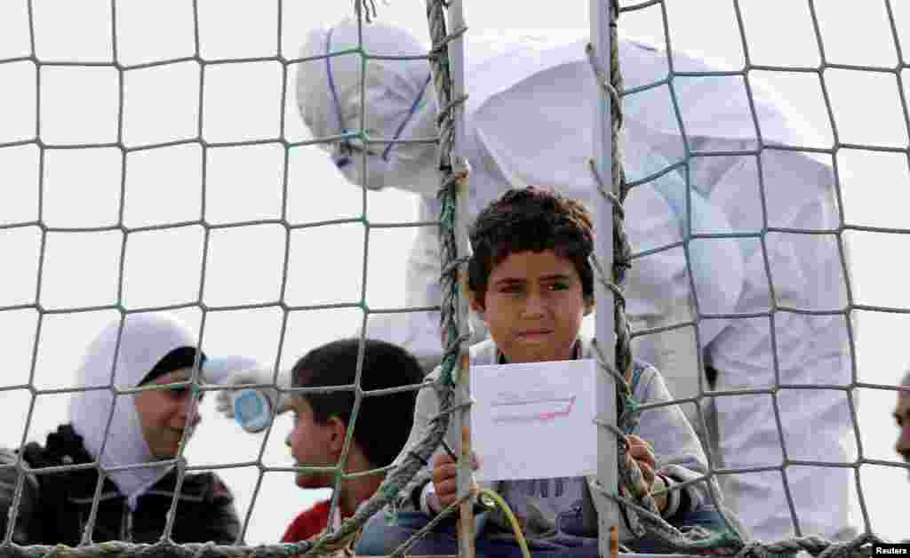 A Syrian child holds a drawing as he waits to disembark from Belgian Navy vessel Godetia at the Augusta port, Italy, on June 10, as around 250 migrants from Syria arrived at the Sicilian harbour from a Damascus refugee camp. (Reuters/Antonio Parri)