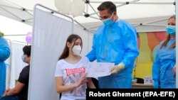 România: vaccinarea tinerilor de la 12 ani. Ana, în vârstă de 14 ani primește o diplomă de vaccinare anti Covid-19 de la șeful campaniei naționale de vaccinare, Valeriu Gheorghiță. 