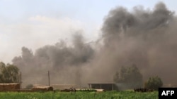 Members of the Kurdish peshmerga forces walk in a field as smoke billows in the background following clashes with IS jihadists during a large operation southwest of the oil hub of Kirkuk, in Iraq.