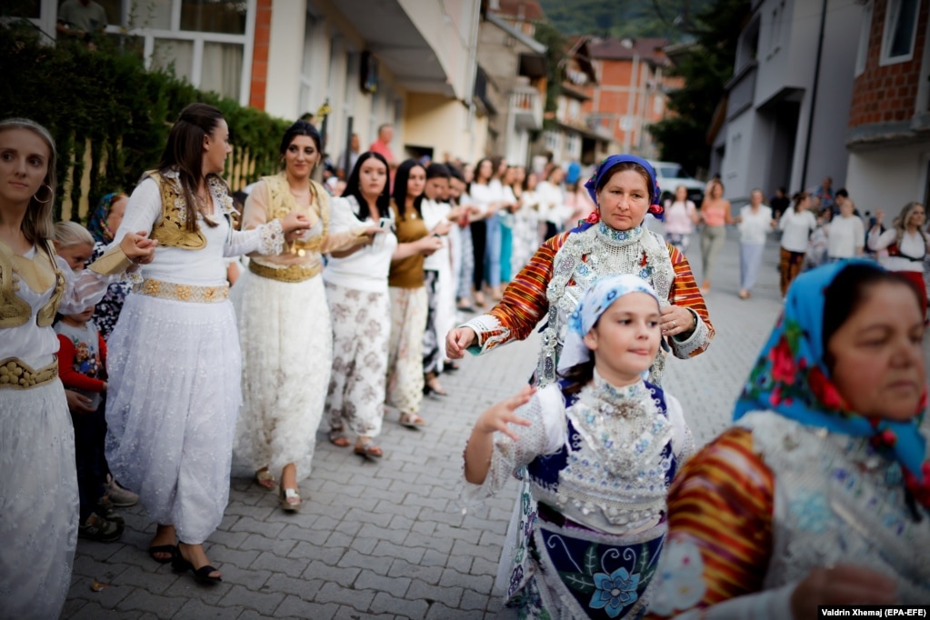 Gratë e fshatit, të veshura me fustane tradicionale, duke vallëzuar në rrugët e fshatit.