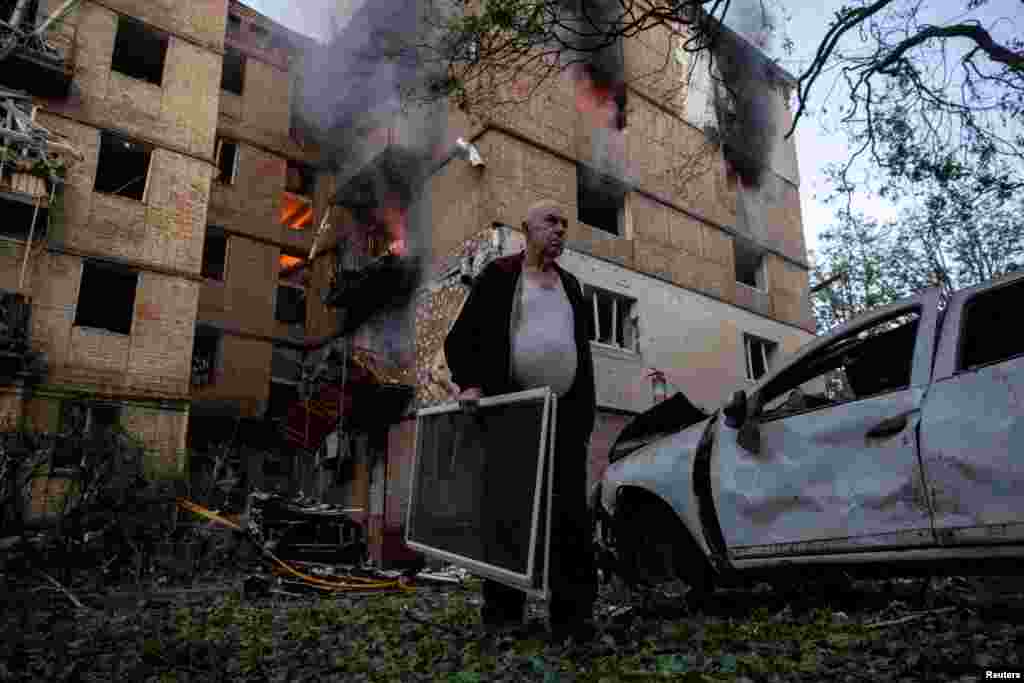 A Kyiv resident carries window screens outside a damaged apartment building that caught fire after a Russian drone strike.