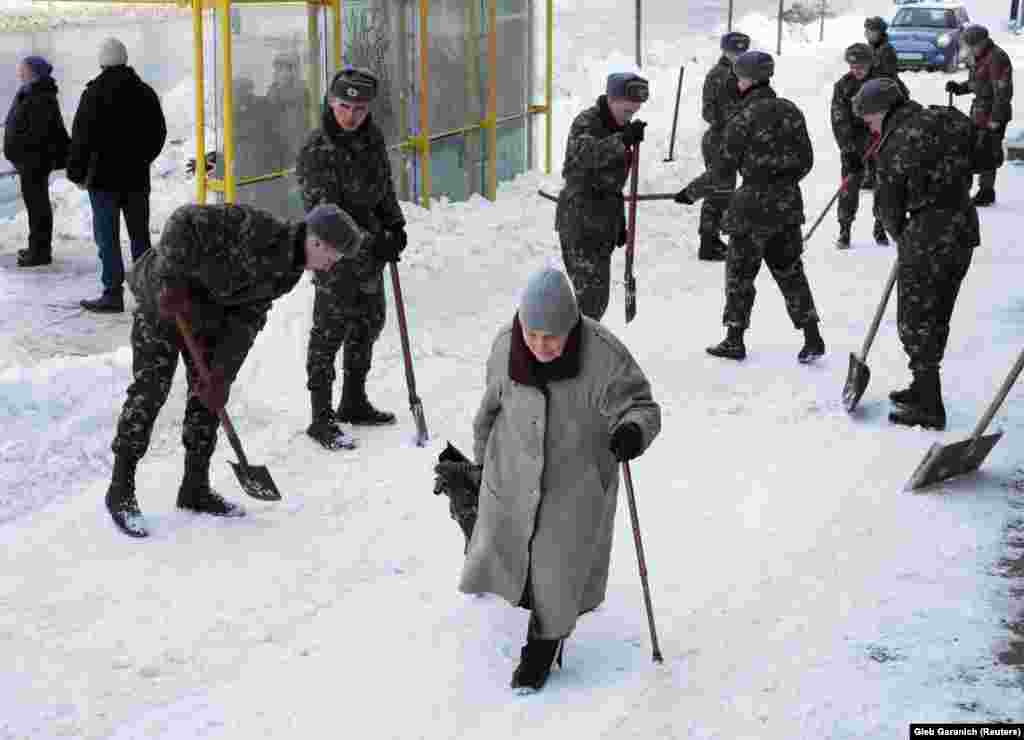 Жанчына праходзіць міма салдат, якія чысьцяць вуліцу ад сьнегу пасьля завеі ў Кіеве 