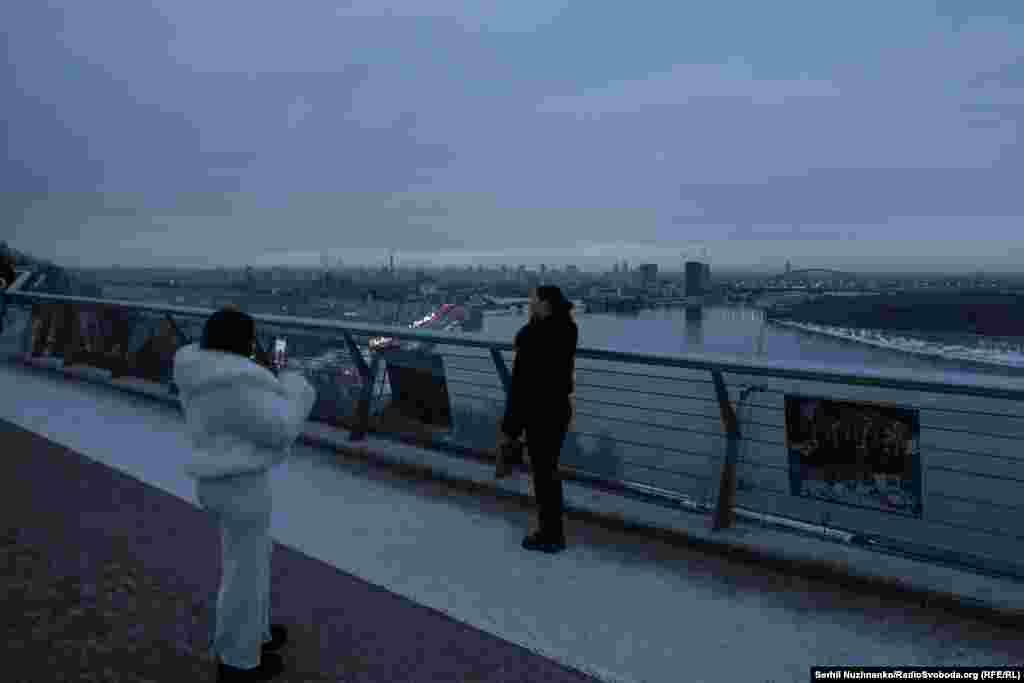 Дівчата роблять фото на скляному мосту. Київ, 24 лютого 2026 року.У цей час чотири роки тому йшли запеклі бої з російськими військами на аеродромі в Гостомелі, близько 30 км звідси