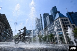 Një burrë nget biçikletën e tij përmes një shatërvani pranë lagjes bankare në Frankfurt, Gjermania perëndimore, më 26 qershor 2026 me temperaturën e ajrit që arrin 39 gradë Celsius.