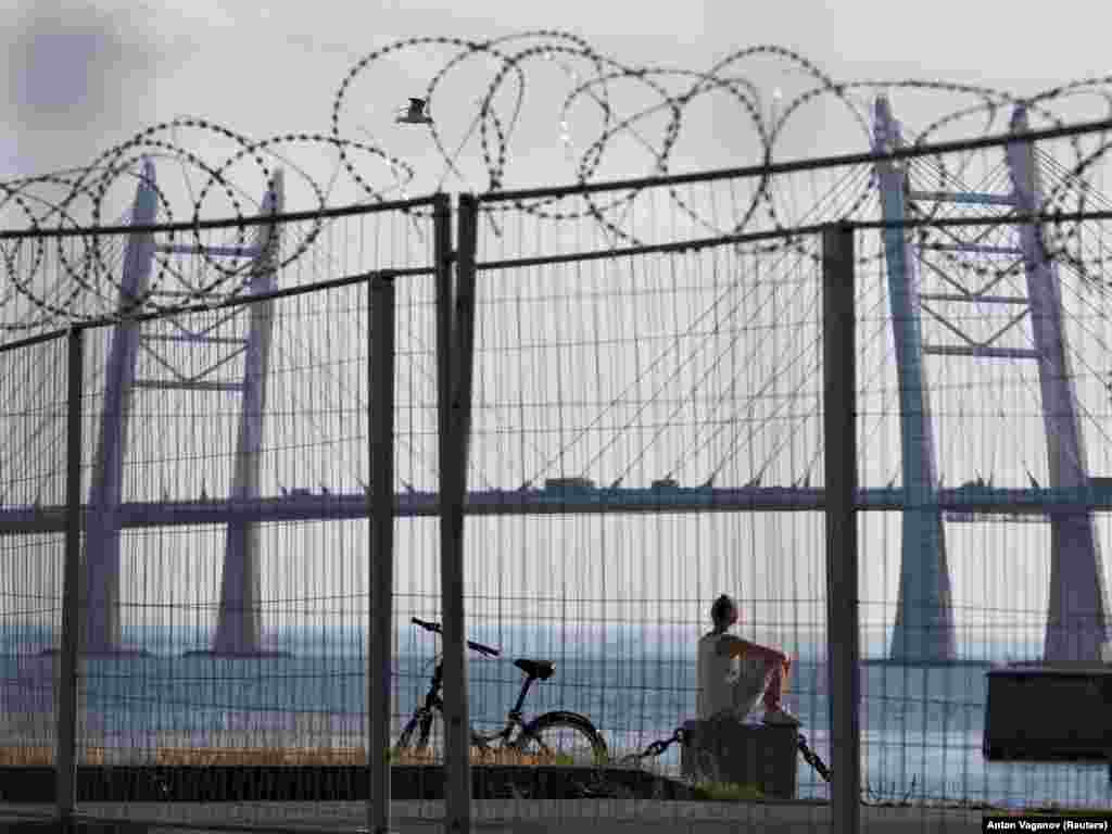 A woman sits by the shore next to the fence of a temporary hospital for patients infected with the COVID-19 in St. Petersburg.&nbsp;