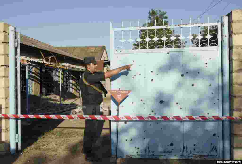 A police officer stands by the gate of a cordoned-off house in the Azerbaijani village of Agdam as sappers deal with an unexploded shell.