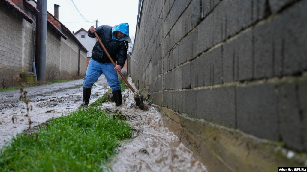 Një qytetar tenton të pastrojë një rrugë të vërshuar në Malishevë.