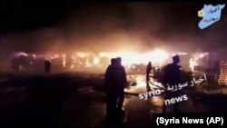 People stand in front of flames rising after an attack on an area known to have numerous Syrian army military bases, in Kisweh, south of Damascus, May 9, 2018