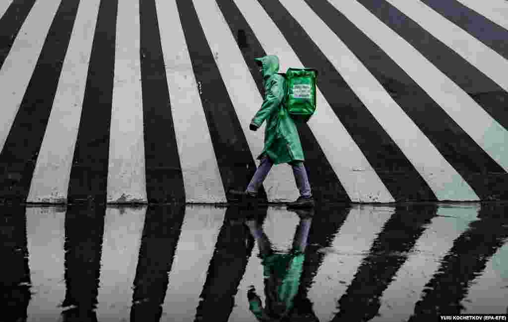 A food delivery man walks in front of a mural during a rainfall in Moscow.