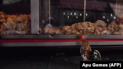 Një gjel duke qëndruar para mishit të pulës, të ekspozuar në një dyqan në Brazil. Fotografi nga arkivi.