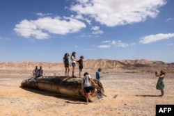 Njerëzit qëndrojnë mbi mbetjet e një rakete iraniane në shkretëtirën Negev, pranë Aradit, Izrael, më 2 tetor.