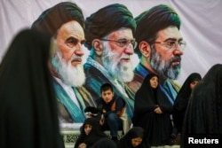 People gather near a banner of Iran's late leader of the Islamic Revolution Ayatollah Ruhollah Khomeini, Iran's late Supreme Leader Ayatollah Ali Khamenei, and Iran's current Supreme Leader Mojtaba Khamenei, on the day of a ceremony at Khomeini's shrine in Tehran on June 4.