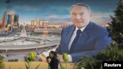 Kazakhstan -- A couple walks past an election banner of Kazakh President and presidential candidate Nursultan Nazarbaev in Almaty, April 21, 2015