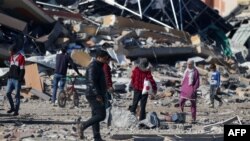 Disa persona duke kaluar pranë një ndërtese të shkatërruar në kampin e refugjatëve, Al-Magazia, në Gazën qendrore më 16 janar 2024. 