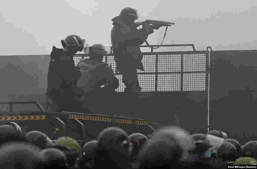 A Kazakh riot policeman aims a weapon at protesters from a barricade in Almaty.&nbsp;