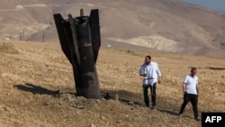 Two Israeli men examine a fallen rock half-buried in the ground on the outskirts of Jericho on June 8 following attacks by Iranian and Iran-backed Houthi rebel. 