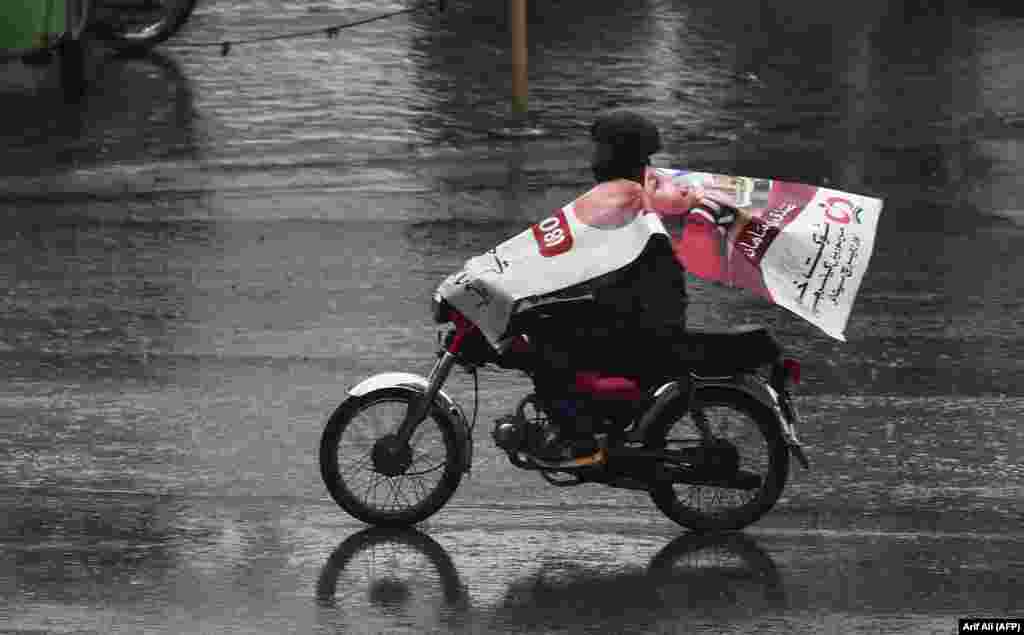 A Pakistani man wears a poster to protect himself from rain as he rides a motorbike in Lahore. (AFP/Arif Ali)