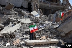 Një burrë duke mbajtur një flamur iranian, mes rrënojave që ka shkaktuar lufta në Teheran.