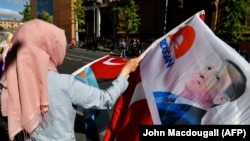 A woman wearing a headscarf waves with a flag with the portrait of Turkish President Recep Tayyip Erdogan near the Adlon Hotel close to the Brandenburg Gate in Berlin, September 27, 2018