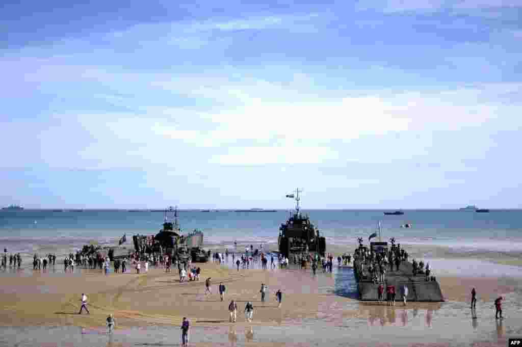 People walk aboard ships set up on the beach in Arromanches prior to a joint French-Dutch D-Day commemoration ceremony on June 6, 2014.