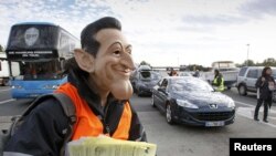 A striking refinery worker, wearing a mask of French President Nicolas Sarkozy, distributes leaflets to drivers during a protest against pension reform at a toll booth near Vienne on October 22.