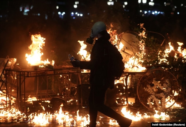 Një protestues i veshur me maskë gazi ecën pranë barrikadave që digjen në Tbilisi, Gjeorgji, 4 tetor 2025.