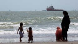 Ljudi na plaži dok se brodovi u Ormuskom moreuzu vide blizu plaže Bandar Abas, Iran, 25. avgust 2026.