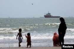 People gather on the beach as vessels in the Strait of Hormuz are visible near the beach of Bandar Abbas, Iran, on August 25.