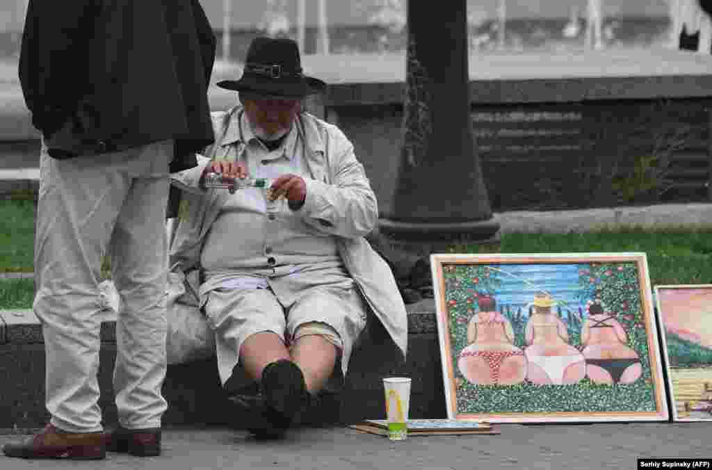A street artist drinks vodka as he sells his paintings to tourists in the center of the Ukrainian capital, Kyiv. (AFP/Sergei Supinsky)