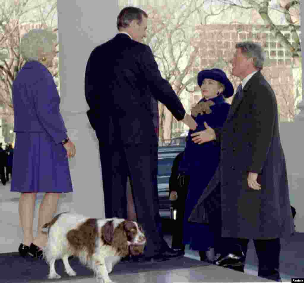 20 января 1993 года. Избранный президент Билл Клинтон (справа) вместе с женой Хиллари Клинтон здоровается с 41-м президентом Джорджем Бушем (слева) и первой леди Барбарой Буш во время визита в Белый дом. Позади Бушей, на переднем плане &ndash; их пес Милли