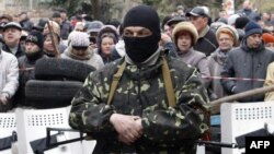 Ukraine - Local residents look on as an armed pro-Russian activist guards a police station in the eastern Ukrainian city of Slovyansk after it was seized by a few dozen gunmen on April 12, 2014. 