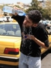 An Iranian taxi driver cools down by splashing water on his face on a street amid soaring temperatures in Tehran on July 22, 2025.