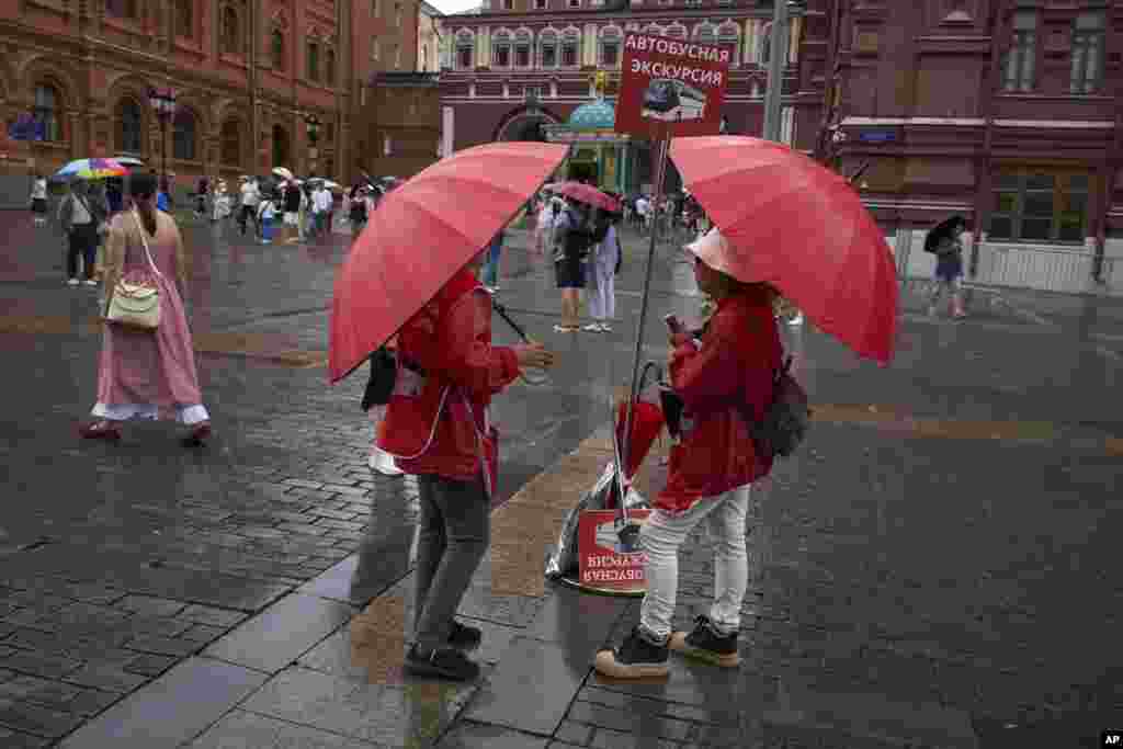 Tour guides talk to each other while waiting for tourists under umbrellas during a rain shower on Moscow's Red Square.