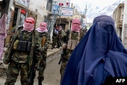 Taliban security personnel stand guard as a burqa-clad woman shops at a street market in Afghanistan's Badakhshan Province in February 2024.