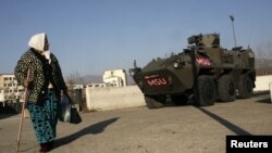 A woman passes by an Austrian KFOR armored vehicle guarding the main bridge in the ethnically divided town of Mitrovica.