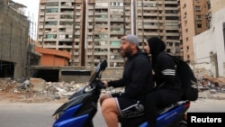 Un cuplu de refugiați se întoarce în suburbiile din sudul Beirutului, trecând pe lângă o clădire avariată, după intrarea în vigoare a unui armistițiu de 10 zile între Liban și Israel. 