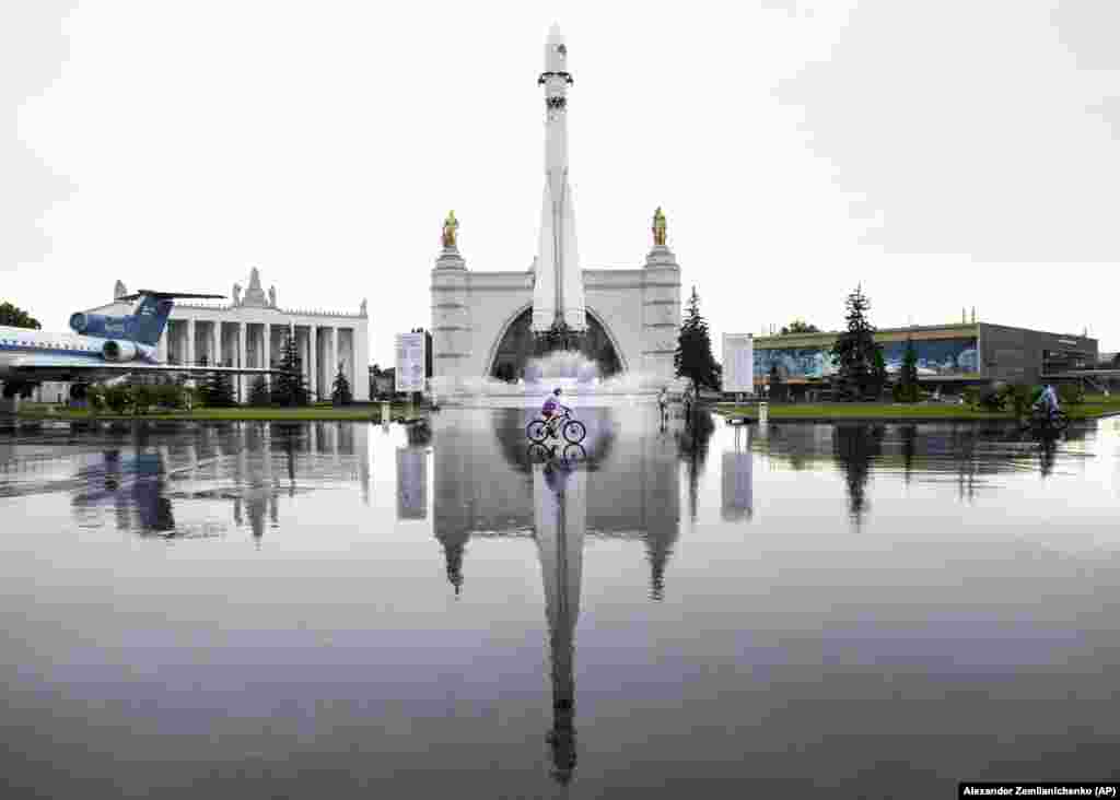 A girl rides a bicycle in front of a fountain and Cosmos pavilion with a Soviet-era Vostok rocket, at the All-Russia Exhibition of National Economy in Moscow. (AP/Aleksandr Zemlyanichenko)