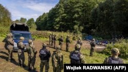 Lengyel és belarusz határőrök egymással szemben a két ország határánál, közöttük illegális határátlépésen ért migránsok
