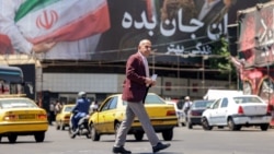 A man crosses a street past vehicles moving near a large political billboard in central Tehran on May 26. 