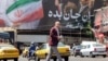 Një burrë kalon një rrugë pranë një billboardi të madh politik përgjatë Sheshit Enghelab në qendër të Teheranit, më 26 maj 2026.